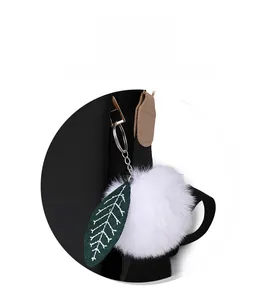 Détail d'un pompon blanc moelleux avec feuille verte sur la fermeture d'un sac à dos noir