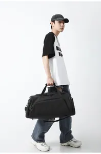 Man carrying a large black duffel bag with a shoe compartment and adjustable shoulder strap