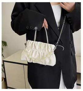 Detail of white pleated handbag featuring a beaded chain and metallic strap accessory