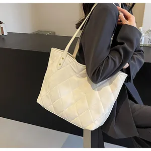 Detailed view of beige quilted tote bag worn with a dark blazer for a stylish commuter look