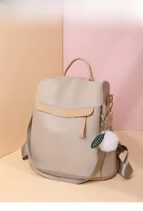 Détail d'un sac à dos en nylon beige avec bordure en similicuir et breloque boule en peluche