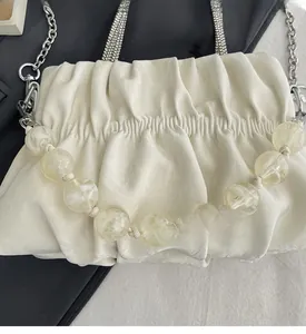 Detail of cream pleated handbag with amber bead strap and silver metal chain accessory