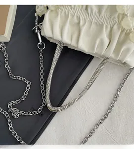 Detail of white pleated handbag with rhinestone strap and large amber bead accents