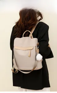 Vue arrière du sac à dos antivol beige pour femme avec pompon blanc et cuir élégant