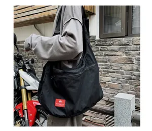 Detailed outdoor view of black canvas crossbody bag featuring a red logo patch
