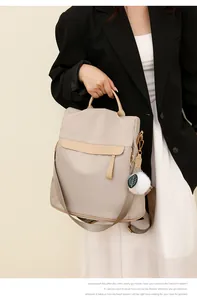 Détail du sac à dos en nylon beige avec rabat en cuir et pendentif pompon blanc élégant