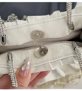 Detail of silver magnetic closure on white pleated bag with shiny synthetic leather