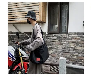 Street view of black canvas crossbody bag with adjustable strap and red logo tag