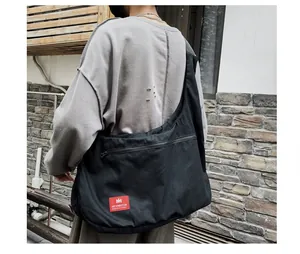 Detail of black canvas crossbody bag with red HEYMISTER logo and front zipper pocket