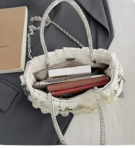 Detail of white pleated handbag with rhinestone handles and spacious interior storage