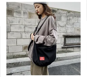 Detail of black canvas messenger bag featuring red logo tag and comfortable wide strap