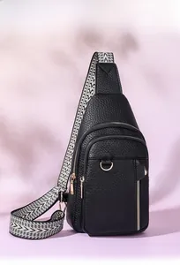 Close-up of black litchi pattern leather sling bag with geometric woven strap and gold zippers