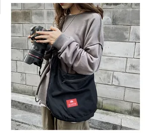 Detail of black canvas crossbody bag with red logo patch and zipper pocket in outdoor setting