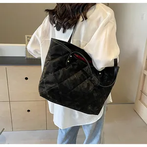 Close-up of black quilted tote bag with red lining and slim shoulder straps on a model