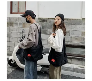 Detail of a large black canvas messenger bag featuring a red logo patch and casual style