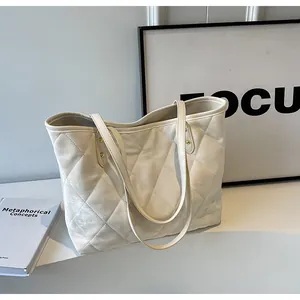 Detailed view of cream white tote bag with diamond quilted pattern and metal rivet accents