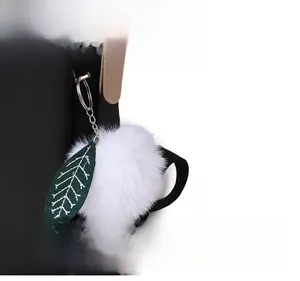 Détail d'un sac à dos en nylon noir avec un pompon blanc et un charm en forme de feuille