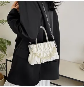 Close-up of white ruched cloud bag with elegant pearl handle and silver chain strap
