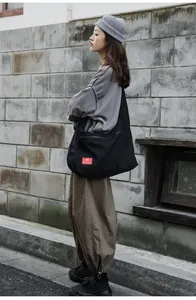 Detail of black canvas messenger bag featuring a red logo patch and spacious side zipper pocket