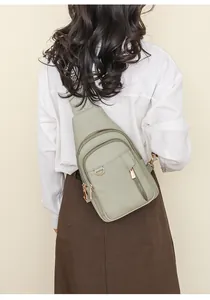 Detail of light green pebbled leather chest bag with multiple zippers and gold hardware