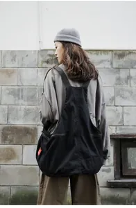 Detail of a black vest-style canvas crossbody bag with shoulder straps and red label tag