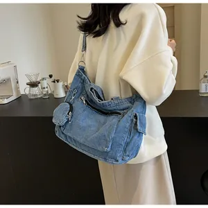 Dettaglio borsa a tracolla in denim blu con tasche utilitarie e un piccolo borsellino