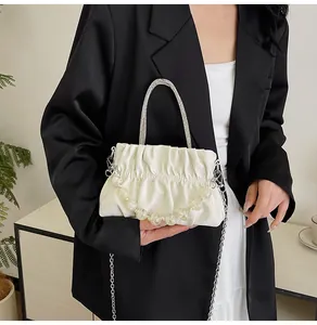 Detail of white pleated handbag featuring a rhinestone handle and beaded chain strap
