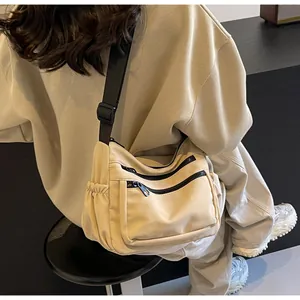 Detail view of beige canvas crossbody bag showing multiple black zippered pockets and strap