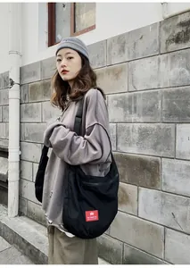 Detail of black crescent canvas shoulder bag featuring red brand label and zipper pocket