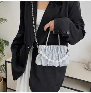 Detail of grey pleated bag with white pearl handle and metal chain on a model