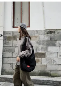 Street style view of a large black canvas messenger bag with adjustable wide strap