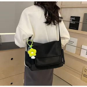 Detail van zwarte nylon schoudertas met voorvak en groene bloemhanger gedragen door model