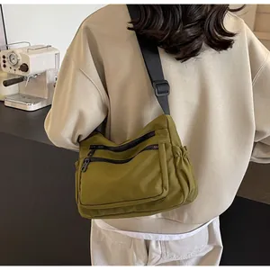 Detail view of olive green nylon crossbody bag with multi-zipper pockets and wide strap