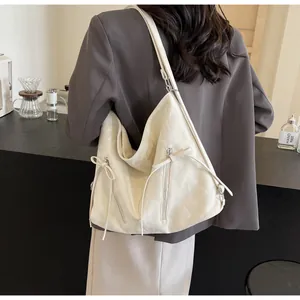 Detail view of cream leather hobo bag featuring decorative zippers and long fringe tassels
