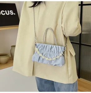 Light blue pleated crossbody bag detail showing silver chain and beaded handle on a model