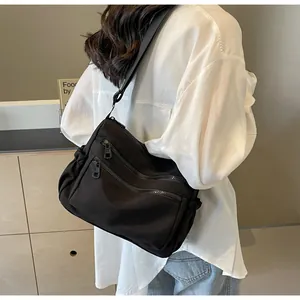 Detailed view of black nylon crossbody bag featuring multi-zipper layers and side drawstring