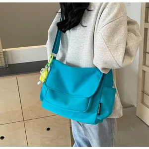 Detail van blauwe canvas schoudertas met verstelbare riem en zijzak gedragen door model