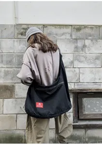 Detail of a black high-capacity canvas crossbody bag with red logo tag on street background