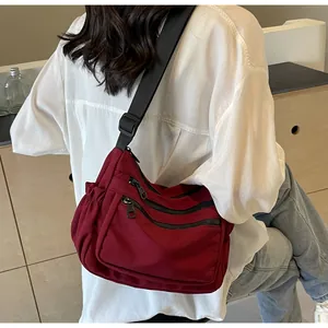 Detail of burgundy nylon crossbody bag with three front zippers and ruched side on model