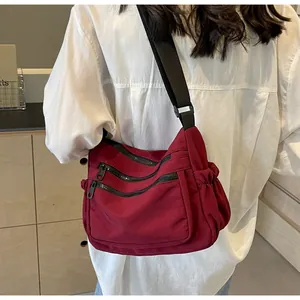 Detail of burgundy nylon crossbody bag with three zipper pockets and adjustable strap