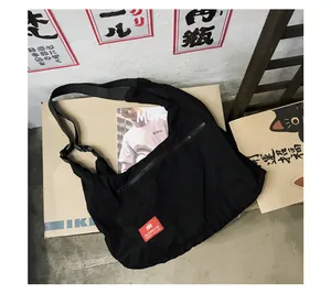 Detail of black canvas messenger bag featuring a red logo tag and adjustable strap