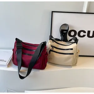 Detail of burgundy and beige nylon crossbody bags with multi-pocket design and zippers
