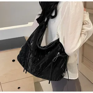 Detailed view of a black tote bag featuring glossy crinkled fabric and ribbon accents
