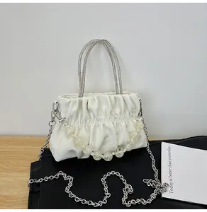 Detail of off-white pleated handbag with silver metal handles and beaded decorative chain