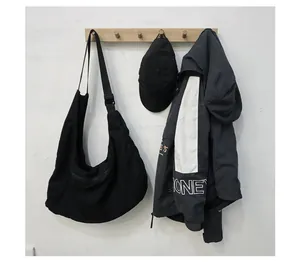 Detail of a black large-capacity canvas messenger bag with adjustable wide strap on a hanger