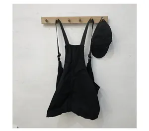 Detail shot of a black cotton jumpsuit and matching baseball cap on a wooden hook