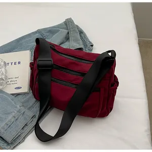 Detail view of burgundy nylon crossbody bag with multiple zip pockets and wide black strap
