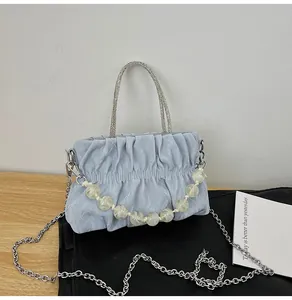 Detail of light blue pleated handbag featuring silver bead handles and pearl chain accent