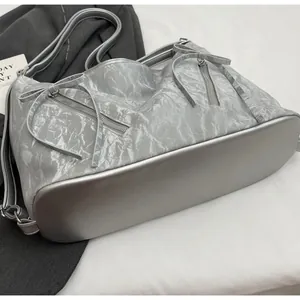 Close-up of silver-gray tote bag with wrinkled texture, metal zippers and bow details