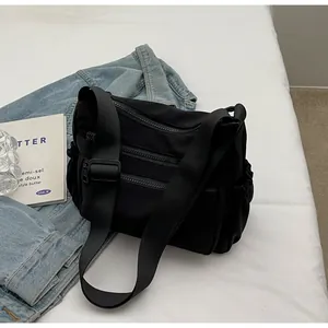 Detail view of black nylon multi-pocket crossbody bag with wide strap on light background